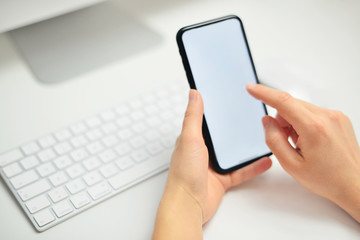 Top view Woman hand Using a Smartphone in office with white screen. Desk with white keyboard.