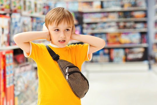 Kid Makes Difficult Choice In Supermarket. Сhildren's Tantrum In The Store. Many Toys Around. Shop Toys.