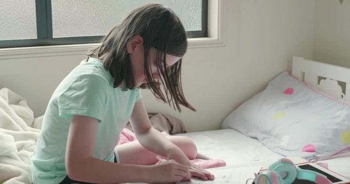 young girl home schooling or doing homework in her bedroom. She is writing in a notepad at a small table, then she uses an eraser to rub out what she has written