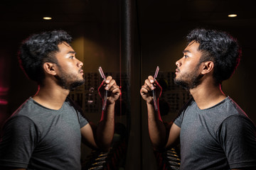 Portrait of black Asian man with beard short hair wear grey shirt shave facial by razor looking reflection in mirror on fitness background stock photo