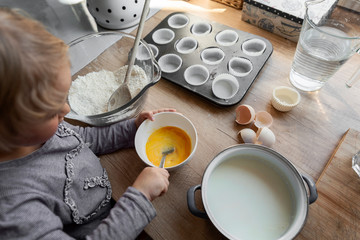 Little child making cookies, mix egg and prepare dough for homemade dessert and muffins. Chef in the kitchen with raw ingredients for dessert. Close up.