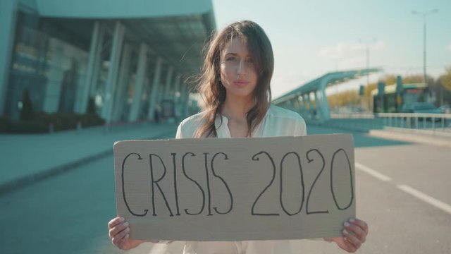 Crisis 2020. Caucasian beautiful serious woman showing an invocatory banner standing near an airport. Action protest against economic disaster during quarantine.