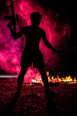 silhouette of black Asian man topless, sport plant and sneaker holding rifle in right hand with red fire background  stock photo