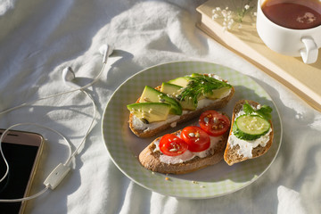 Plate with sliced avocado  and tomato on toast bread with spices on bed at breakfast time
