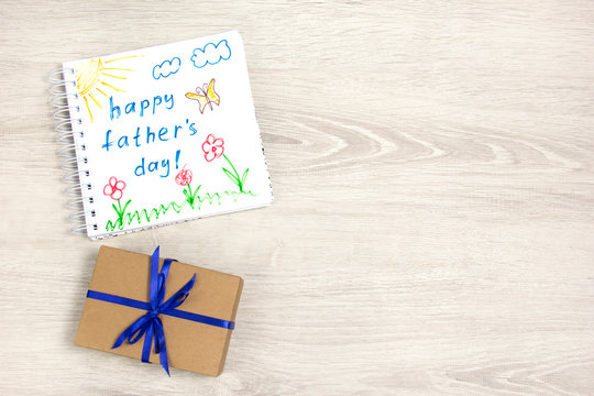 Child's drawing of happy father's day using crayonChild's drawing of happy father's day using crayon. Gift box with blue ribbon.