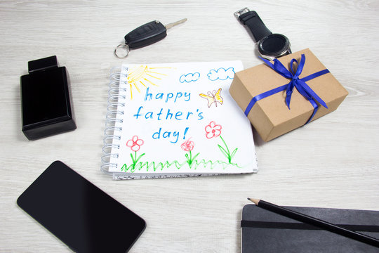 Childrens drawing. Fathers day, mens accessories. Flat view. The drawing is on the table next to the clock, Notepad, keys, smartphone.