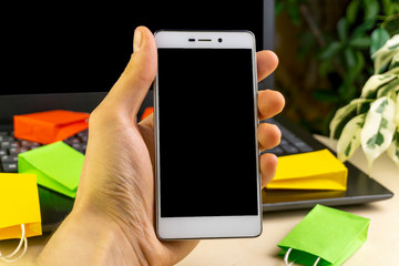 online shopping concept.Hand hold smartphone, boxes, colorful bags, bank card, dollars stand on laptop
