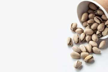 A bunch of pistachios poured out of the little pot. Copy space.