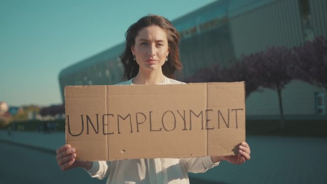 Serious young caucasian woman protests against unemployment holding a strike banner standing outside business building. Crisis 2020. Job loss during quarantine.