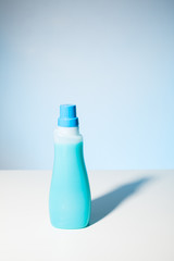 Single blue detergent bottle with blue screw cap against a pale blue bakcground.