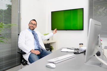 man male doctor professor teacher in medical office at desk with computer wearing white lab coat showing to students wall green srceen research covid19 and coronavirus seminar