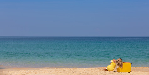 Fototapeta na wymiar Beautiful girl in a yellow dress on the beach with a yellow suitcase. Blue sea. Yellow sand
