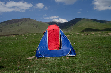 Orange tent on green grass in the mountains in summer
