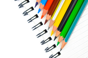 Some different color wood pencil crayon placed on top of a white spiral note book
