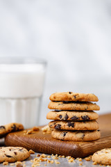 A stack of chocolate chip cookies on a wooden cutting board and a glass of milk on a marble table. White background with empty place for text