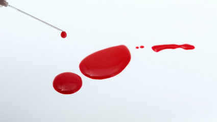 Red liquid dripping from a syringe, like blood, on a white background