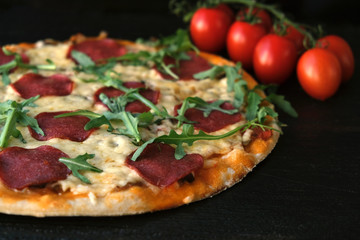 homemade pizza on a dark rustic background, next to a branch of tomatoes and arugula greens.
