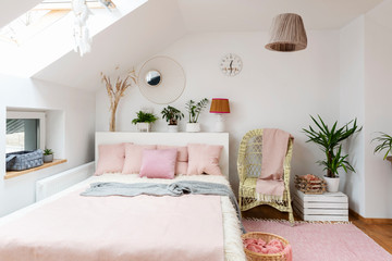 White interior of bedroom in the attic with double bed with pink stylish pillows. Room hotel with modern decor, window and space
