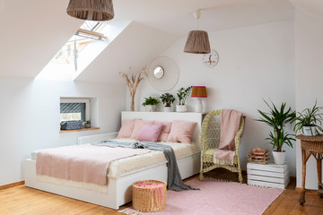 Bedroom with bed in cozy interior in white and pink color. Scandinavian style in room in the attic with double bed. 