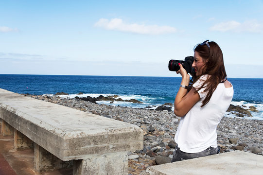 Young brunette woman taking pictures at the seaside