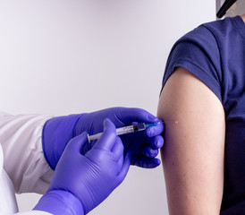 A medical worker in a white coat vaccinates a patient in the shoulder