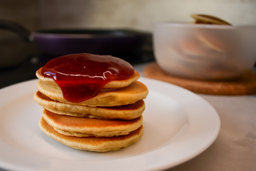 Fototapeta na wymiar Pancakes with berry jam on top on a white plate on a kitchen background.
