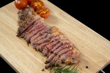 Slice Juicy grilled steak medium rare beef on wooden cutting board with tomato and rosemary , black background  - Stock photo
