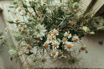Bouquet of wildflowers (chamomiles). Stand on a white windowsill at the window in the room. 
Macro. View from above.
