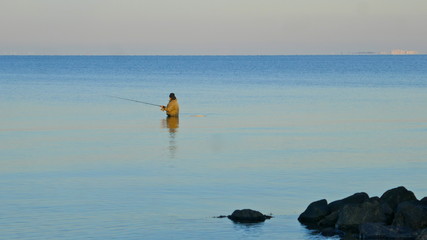 In the afternoon, a male angler stands patiently in the cold water of the Baltic Sea. Hohwacht...