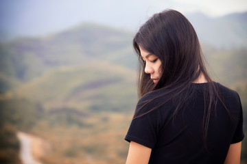 Portrait of asian girl are standing on the moutain to watch the sunset with blurred of green background. Beautiful asian women in black shirt is  sad.