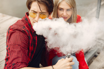 Stylish couple in a city. Two people use the electronic cigarette