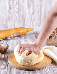 Hands kneading yeast dough on a cutting board on white table