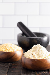 Bowls of Whole Millet and Millet Flour in Wood Bowls on a Dark Table