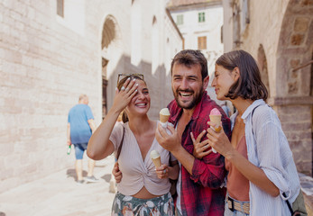 Smiling friends eating ice cream and walking on street