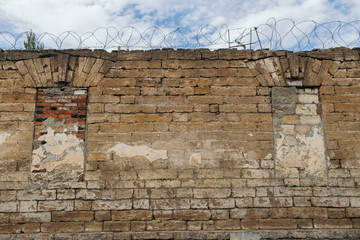 texture of an old wall with blocked Windows with barbed wire against the sky