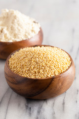 Whole Millet and Millet Flour in a Wood Bowl on a White Marble Countertop