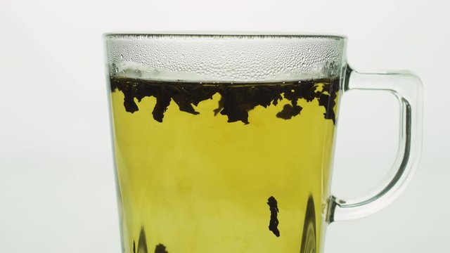 black tea particles floating in a transparent glass mug creating a whirlpool, brewing tea close up .