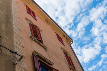 Unusual look at the old italian building with cloіed window shutters and blue cloudy sky on the background