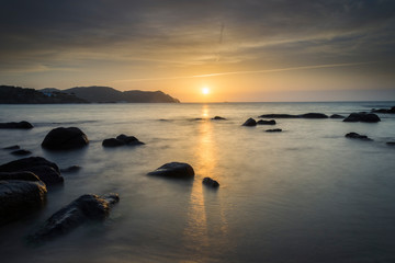 Sun on the horizon of a beach with rocks