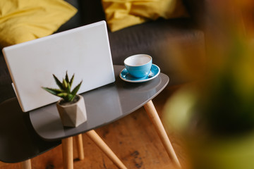 Close up of a  laptop, a cup of coffee and a plant on the table