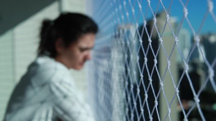 Woman standing in balcony looking at city view. Apartment fence net prevention security