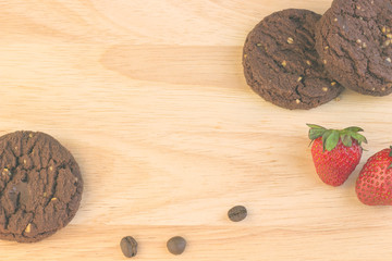 Chocolate cookies, coffee beans, cinnamon sticks and strawberries are on the wooden table.
