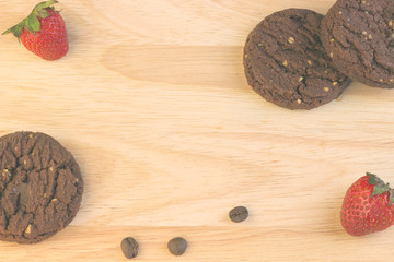 Chocolate cookies, coffee beans, cinnamon sticks and strawberries are on the wooden table.
