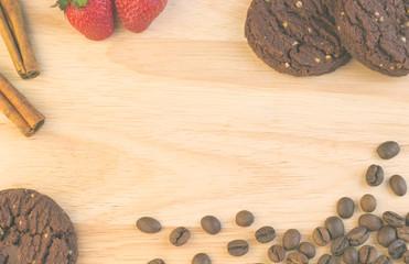 Chocolate cookies, coffee beans, cinnamon sticks and strawberries are on the wooden table.