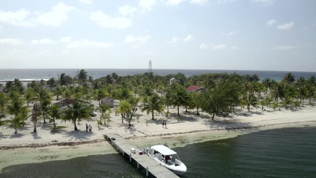 Aerial: Drone reversing from couple standing on shore at beach, people on vacation at island during sunny day - Coco Plum Cay, Belize