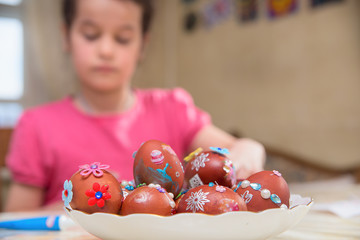 Easter eggs are in a large plate. In the background is a girl with dark hair.