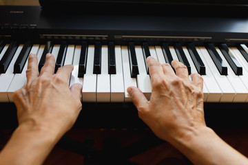 Hands of an old woman playing piano in a house in front of a window