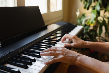 Hands of an old woman playing piano in a house in front of a window