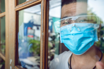 Asian man is wearing surgical mask look outside the window during covid19 or corona virus spread