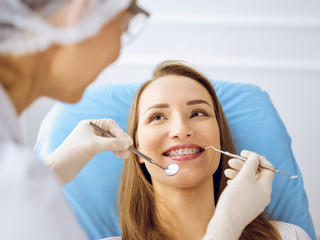 Smiling young woman with orthodontic brackets examined by dentist at dental clinic